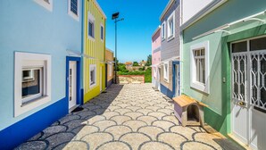 A narrow street with colorful buildings, a tiled pavement, and a clear blue sky. - House (Porto)