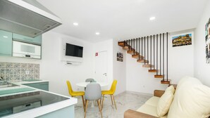 A modern kitchen with a built-in microwave, a dining area with a round table and two chairs, a sofa, and a wooden staircase. - House (Porto)
