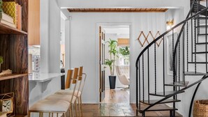 Un interior moderno con una escalera, suelo de madera y una zona de estar con sillas y una mesa.