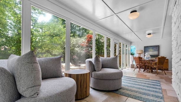Una sala de estar moderna con sofás grises, una mesita redonda de madera y un comedor con sillas de mimbre.