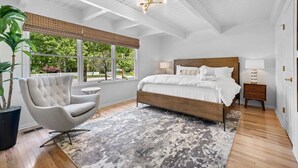Un dormitorio con una cama grande, una silla, una mesita de noche y una ventana con persianas.
