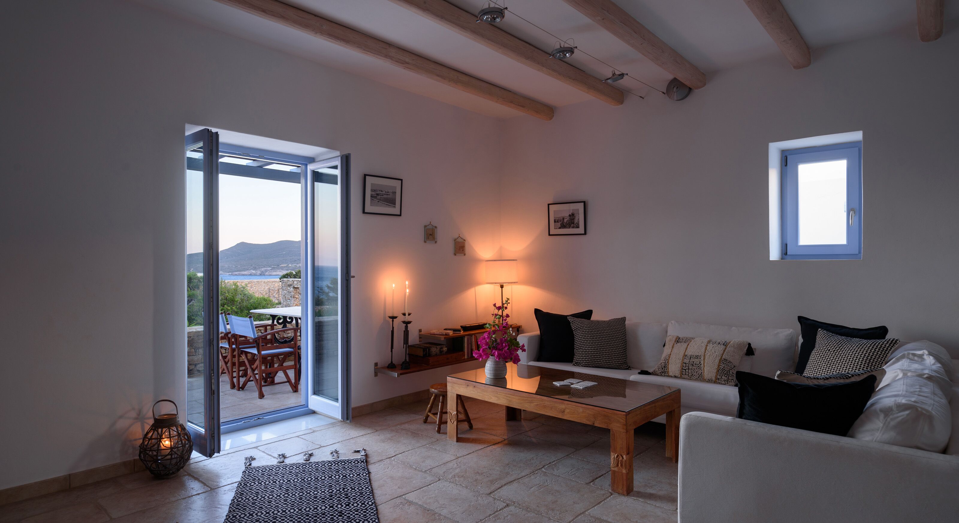 A living room with a white sofa, a coffee table, a lamp, and a view through a glass door to an outdoor patio with a table and chairs.