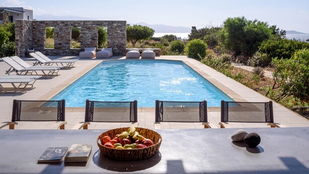 Un espace aménagé au bord de la piscine, avec des chaises longues, un mur en pierre et une vue sur la mer.