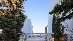 Un escalier en pierre mène à un bâtiment blanc orné d’une balustrade bleue, le tout étant entouré d’arbres et de plantes.
