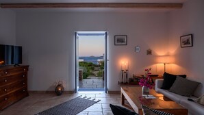 Un salon avec un téléviseur, une commode en bois et une vue sur l’extérieur, grâce à une porte ouverte.