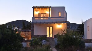 Une maison moderne à deux étages, dotée d’une façade en pierre, d’une entrée centrale et d’un petit balcon à l’étage supérieur.