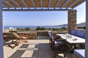 Eine Terrasse im Freien mit Steinmauern, Holzmöbeln und Blick auf das Meer.