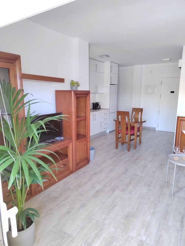 A modern living room with a wooden entertainment unit, a dining area with a table and chairs, and a kitchen in the background.