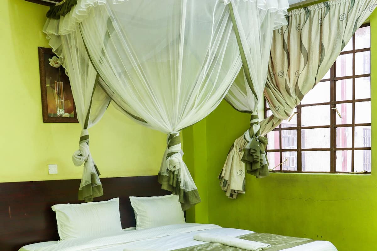 A bed with a canopy, green walls, and a window with curtains.