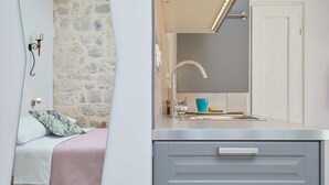 A modern bathroom with a stone wall, a sink with a mirror, and a bed with a pink bedspread and a patterned pillow. - Studio Nikol (Dubrovnik)
