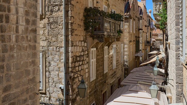 A narrow street with stone buildings, a sloped roof, and a clear blue sky. - Studio Nikol (Dubrovnik)