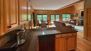 A wooden cabin interior with a kitchen, dining area, and living space. - Yonah View Lodge - 2 BR Cabin w/ Spacious Decks, Hot Tub, Fire Pit, Near Helen (Cleveland)