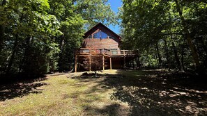 A cabin with a wooden deck, surrounded by trees.