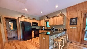 A kitchen with wooden cabinets, a black refrigerator, a microwave, a stove, and a bar area with stools. - Yonah View Lodge - 2 BR Cabin w/ Spacious Decks, Hot Tub, Fire Pit, Near Helen (Cleveland)