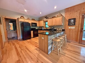 A kitchen with wooden cabinets, a black refrigerator, a microwave, a stove, and a bar area with stools.