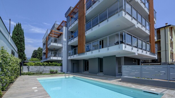 A modern multi-story residential building with balconies, a swimming pool, and a landscaped garden.