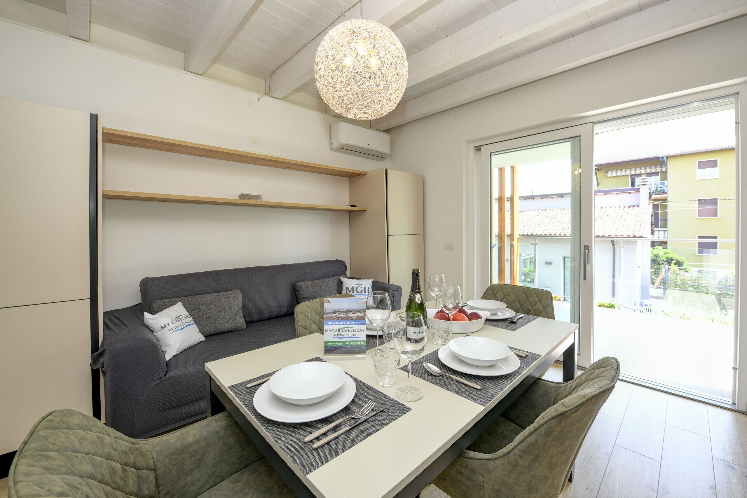 A modern dining area with a table set for four, a grey sofa, and a hanging light fixture.