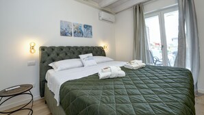 A neatly made bed with a green quilt, white linens, and two pillows. There are two wall-mounted light fixtures on either side of the bed.