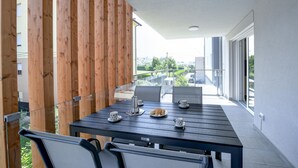 A balcony with a table set for two, featuring a coffee pot, cups, and pastries.