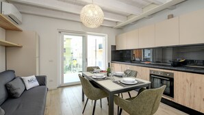 A modern kitchen with wooden cabinets, a dining table set for four, and a grey sofa with a cushion.