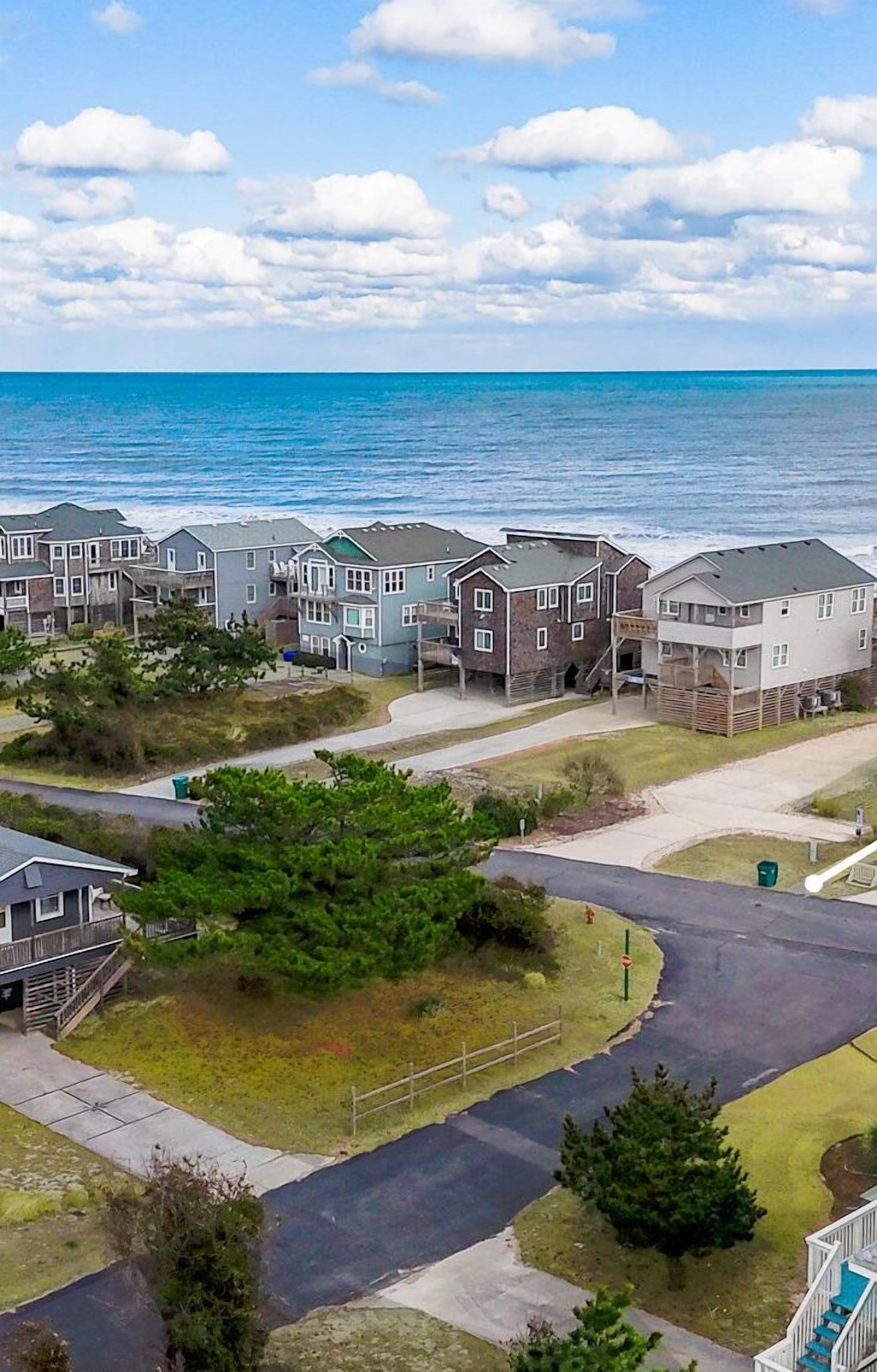 Une zone résidentielle côtière, avec des maisons construites le long du rivage, un ciel dégagé et une vue sur l’océan.