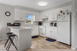 A modern kitchen with white cabinetry, a central island with stools, a built-in oven, a refrigerator, and a clock on the wall.