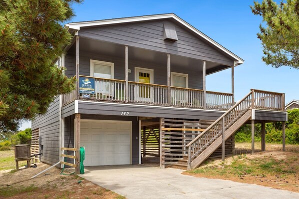A two-story house with a covered porch, a garage, and a staircase leading to the second floor. - Secret Spot: Steps to Beach, Dog-Friendly Duck (Duck)