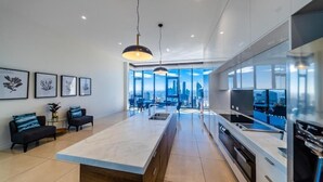 Une cuisine moderne dotée d’un grand îlot central, d’appareils électroménagers intégrés et offrant une vue sur le paysage urbain grâce à de grandes fenêtres.