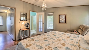 A bedroom with a large bed, a chandelier, a desk with a fan, and a door leading to another room. - Steinhatchee Home w/ Boat Parking: 1 Mi to Marina (Steinhatchee)