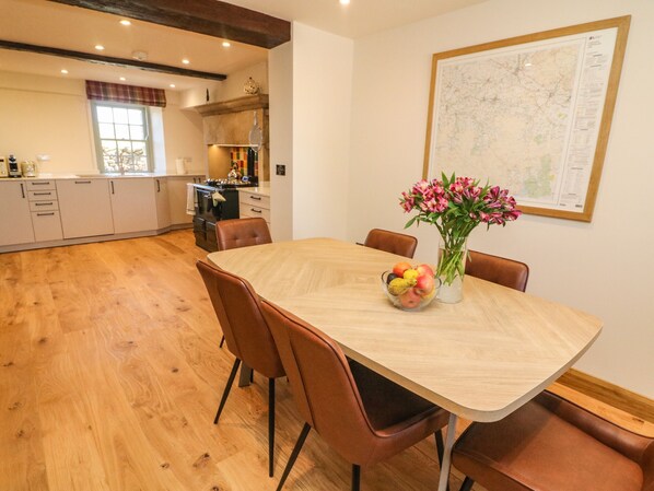 A dining area with a wooden table, brown chairs, a fruit bowl, and a vase of flowers.