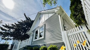 Une maison à l’extérieur blanc, avec un porche à l’avant et un petit jardin fleuri.