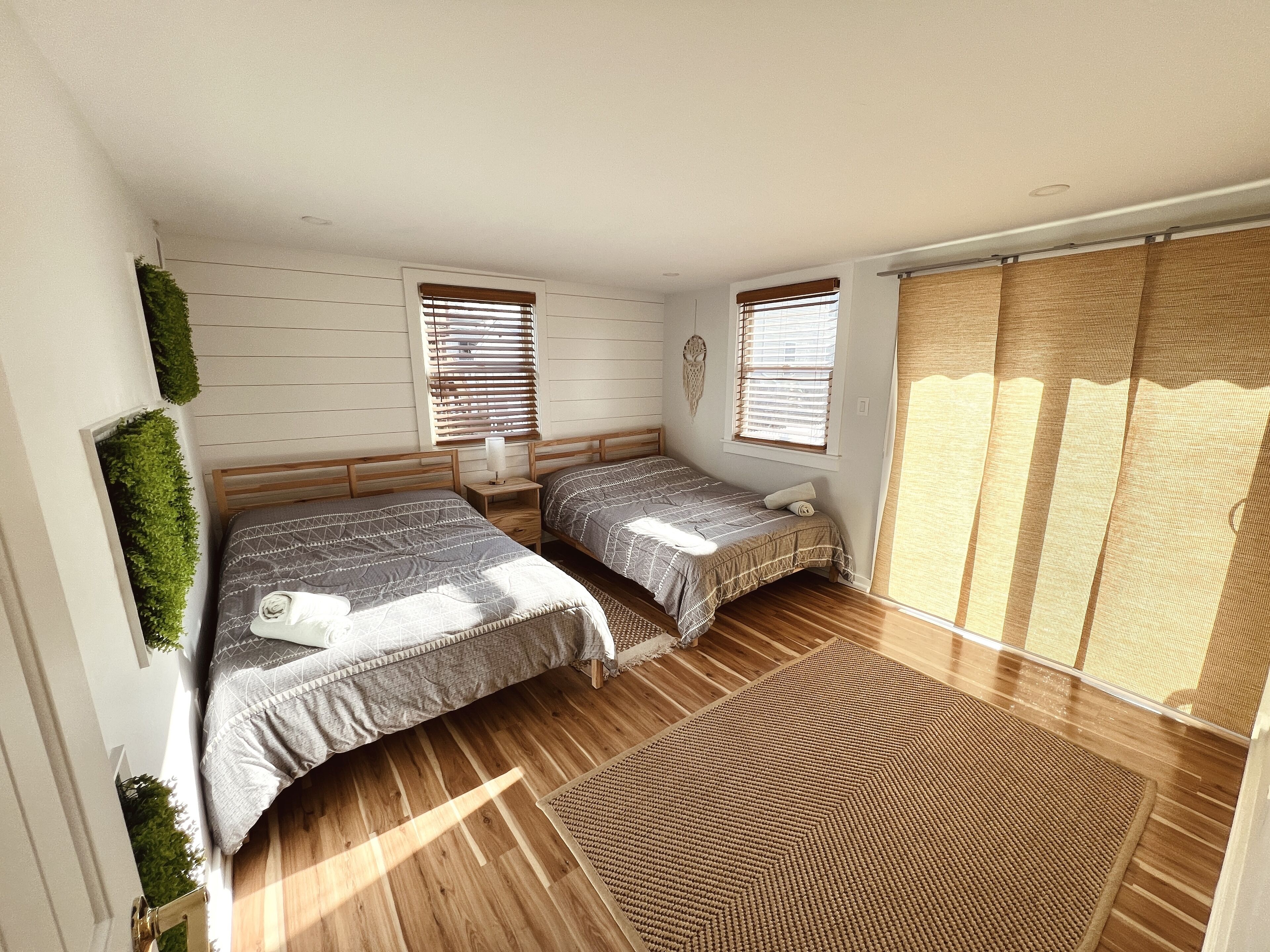 Un dormitorio con dos camas, suelo de madera y un ventanal con persianas.