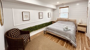 Une chambre à coucher moderne avec un lit, une chaise, une plante fixée au mur et des œuvres d’art encadrées.
