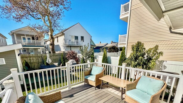 Une terrasse en bois, dotée de meubles en osier et d’une rambarde blanche.