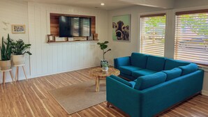 Un salon avec un canapé bleu, un plancher en bois, un téléviseur fixé au mur et des plantes en pot.