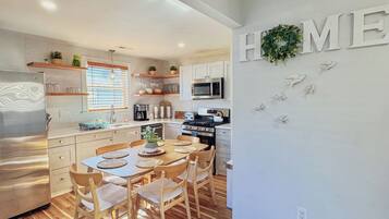 A modern kitchen with white cabinets, a dining table with chairs, and a 'HOME' sign on the wall.