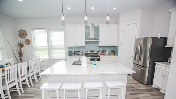 A modern kitchen with white cabinetry, a large island with bar stools, stainless steel appliances, and a herringbone wood floor.