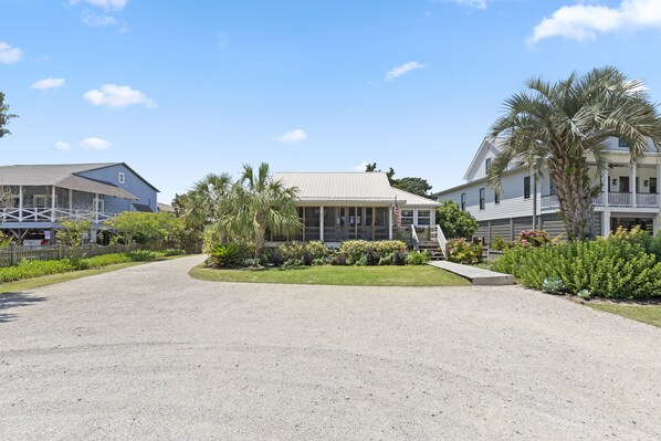 A two-story building with a covered porch, surrounded by a gravel driveway and lush landscaping. - Carolina Kiwi - Off-Ocean, 3-Bedrooms (Pawleys Island)