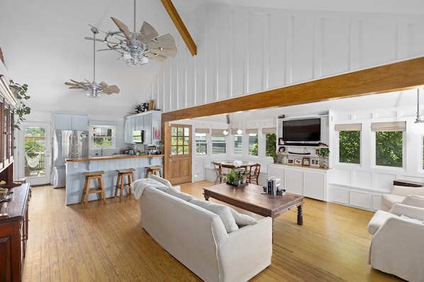 A spacious living area with a wooden ceiling, a kitchen with white cabinets, and a dining area with a TV.