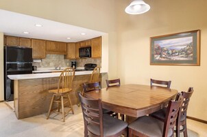 A kitchen with wooden cabinets, a black refrigerator, a microwave, a coffee maker, and a dining table with chairs.