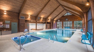 An indoor swimming pool with wooden beams, a changing room, and a view of trees through large windows.