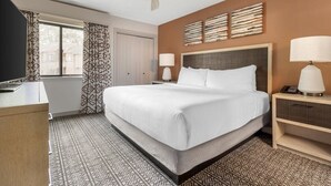 A hotel room with a bed, a desk, a chair, a ceiling fan, a window with curtains, and a wall-mounted lamp. - Fairway Forest Resort (Sapphire)