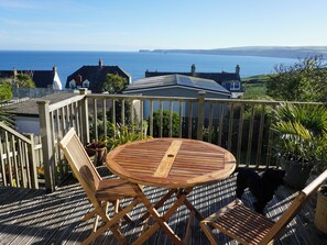 Een houten terras met een ronde tafel en stoelen, met uitzicht op de kust.