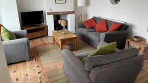 Un salon avec un canapé gris, un téléviseur, une table basse en bois et un tapis à motifs.