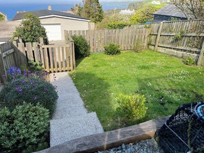 Een achtertuin met een grindpad dat naar een huis leidt, omringd door een houten omheining en diverse planten.