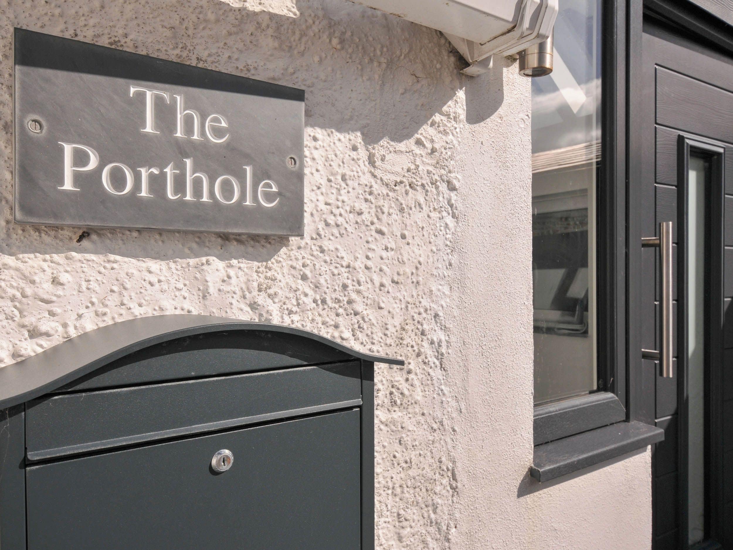 Ein Metallschild mit der Aufschrift 'The Porthole', an einer strukturierten Wand befestigt.
