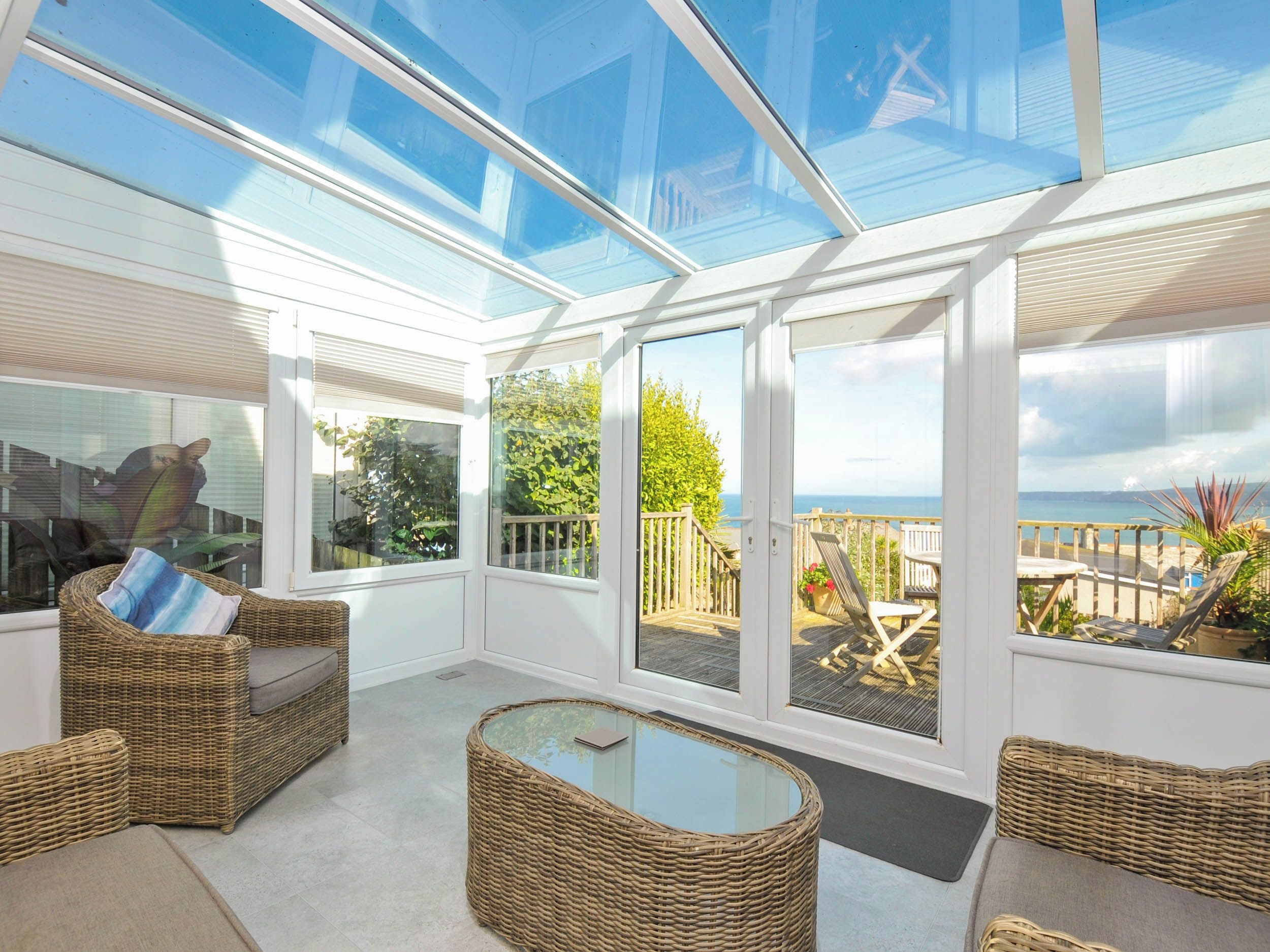 Una habitación luminosa con muebles de mimbre, una mesa de vidrio y vista al mar.