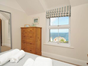 A bedroom with a wooden dresser, a window with a view of the sea, and a bed with white towels. - The Porthole (Port Isaac)