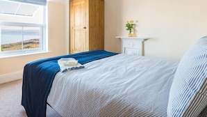 Une chambre à coucher avec un lit, une armoire en bois, une commode blanche, une fenêtre donnant sur un paysage agréable et une petite plante posée sur la commode.