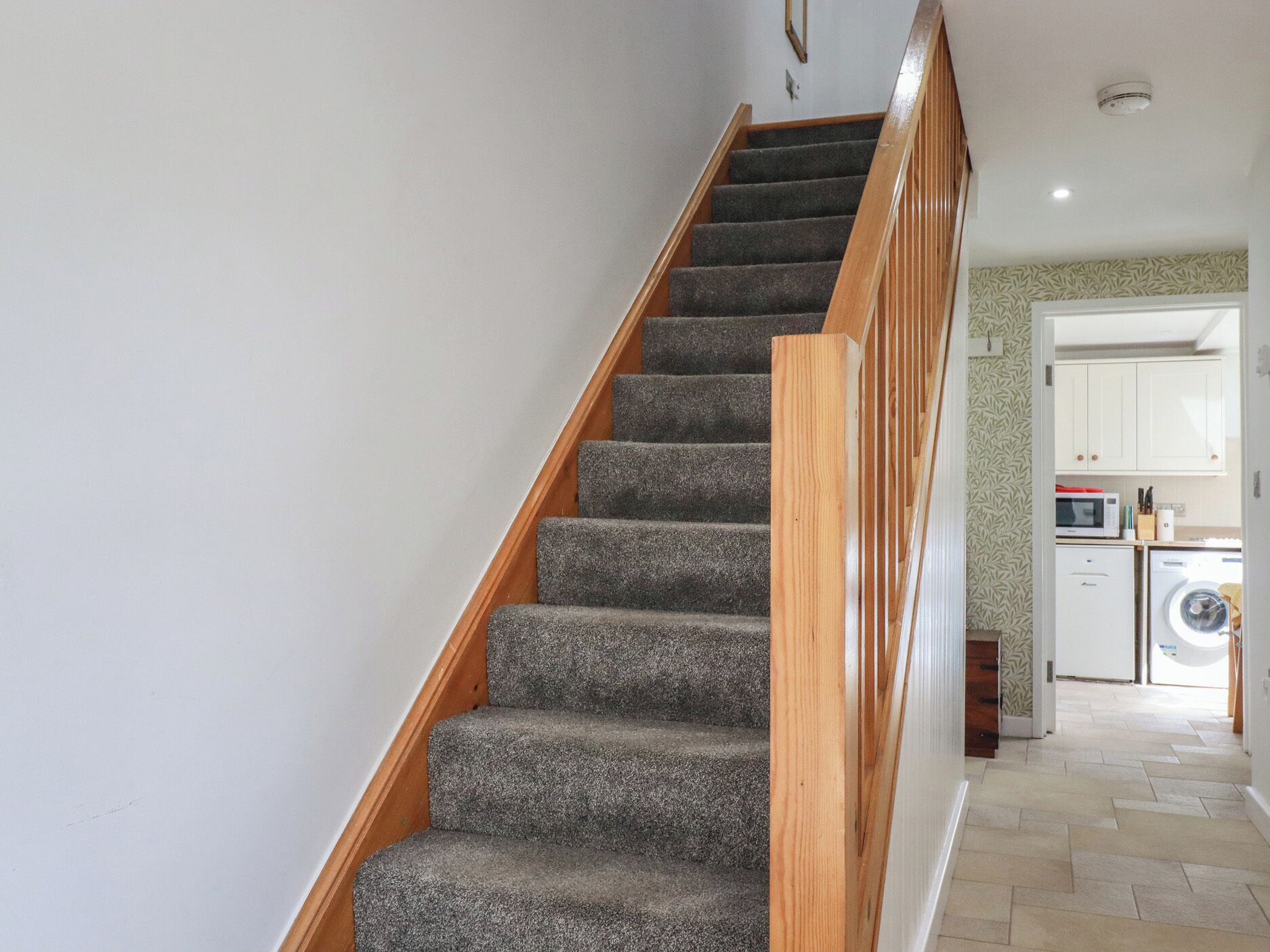 A staircase with carpeted steps and wooden handrails leading to a kitchen area with a washing machine.